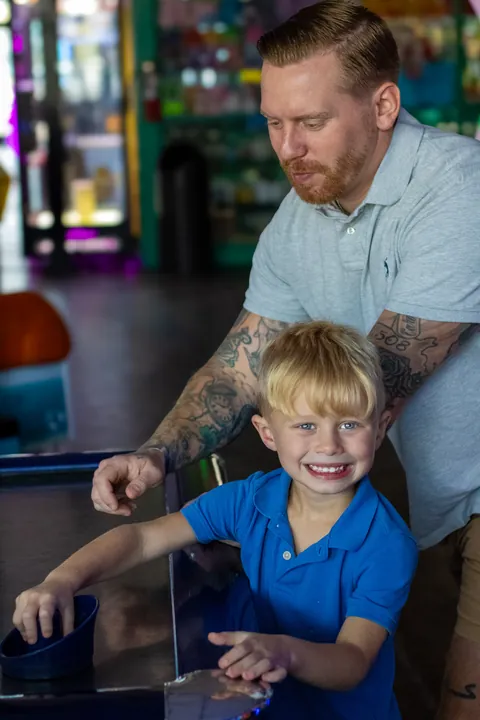 Man helping a smiling boy at an arcade game