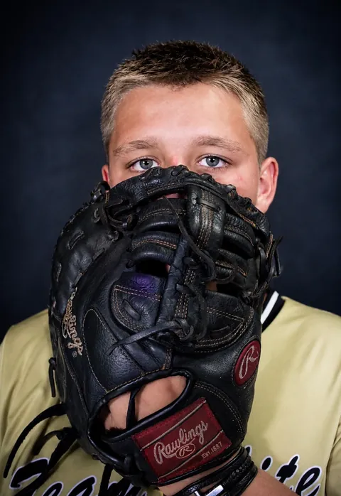 Young baseball player holding his glove over his face