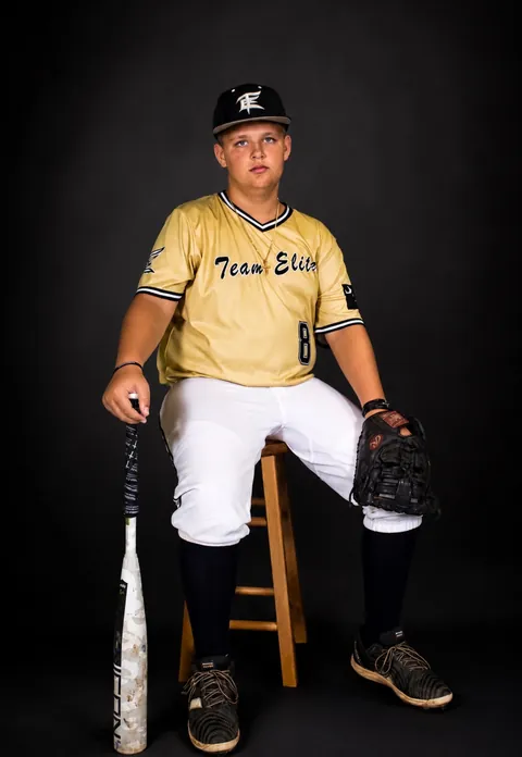 Baseball player seated on a stool with his bat and glove