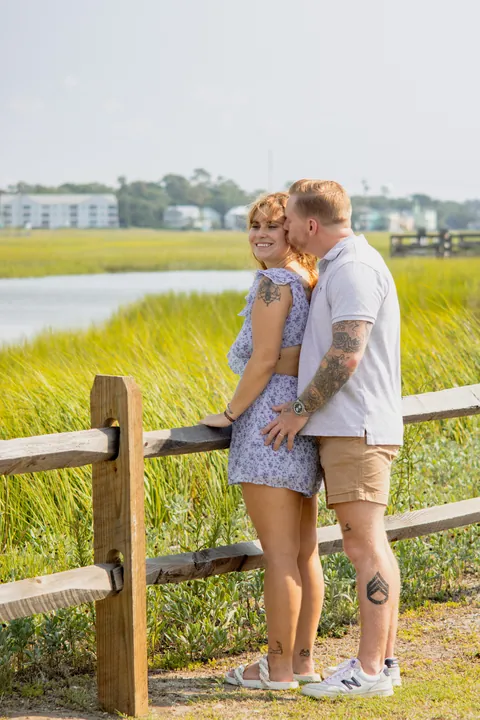 Couple sharing a kiss by a wooden fence at the marsh