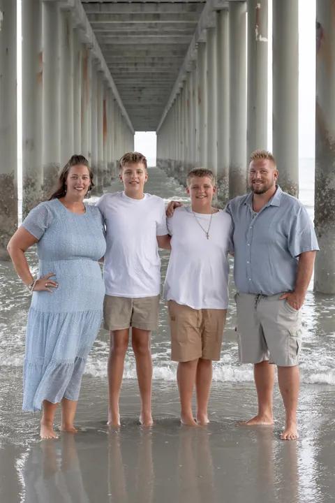 Family of four standing in the shallows under a beach pier