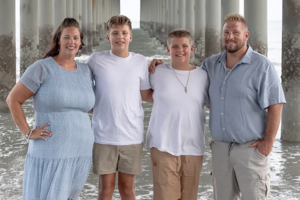 Family of four standing arm in arm under a beach pier