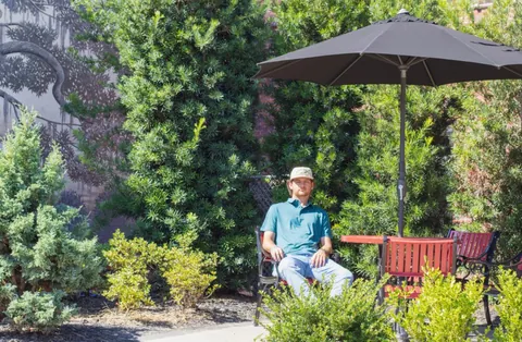 Man seated in a lush garden courtyard under an umbrella