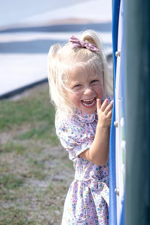 Little girl laughing while peeking around a post