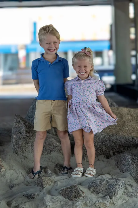 Two young children standing on the rocks under a pier