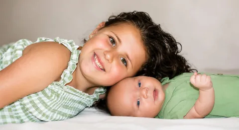 Smiling girl lying cheek to cheek with a newborn baby