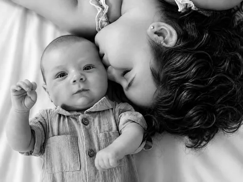 Black and white photo of a girl kissing a newborn baby