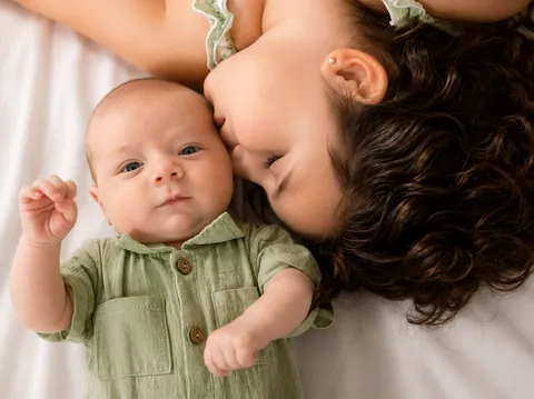 Girl kissing the head of a newborn baby