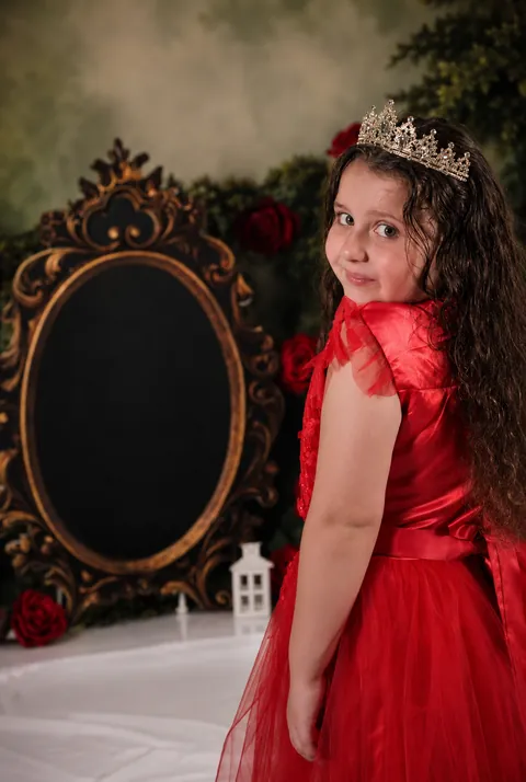 Girl in a red gown and tiara looking back over her shoulder