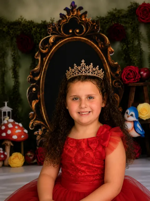 Girl in a red dress and crown in front of an ornate mirror