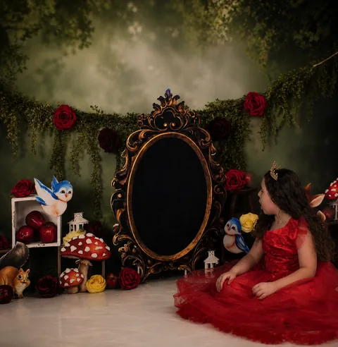 Girl in a red dress seated in a storybook set with roses and mushrooms