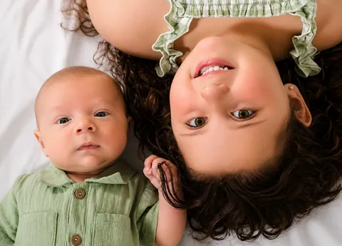 Girl lying upside down beside a newborn baby, both looking up at the camera